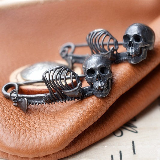 Silver skull and skeleton keychain on a brown leather surface