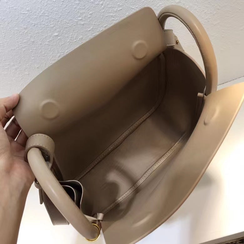 Beige handbag held by a hand against a light background