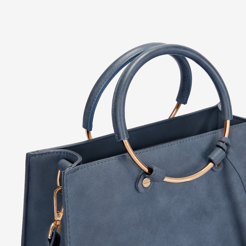 Blue handbag with gold handles and clasps on a light gray background