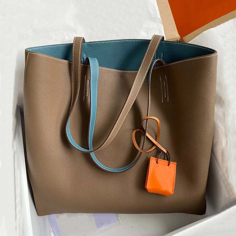Brown leather tote bag with blue interior and orange tag on a white background