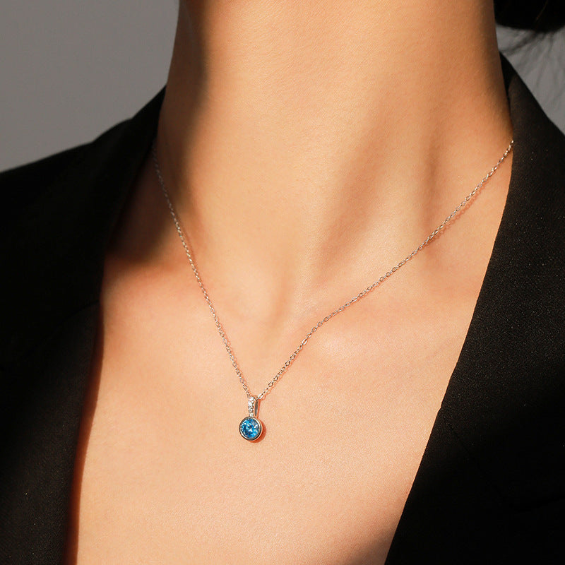 Necklace with a blue gemstone pendant on a person wearing a black top.