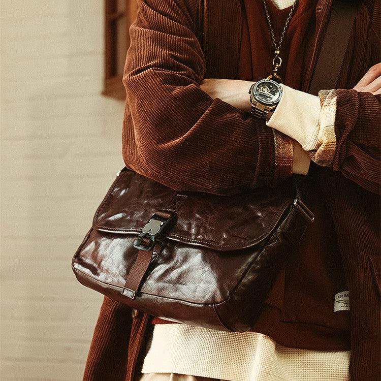 Person wearing a brown jacket holding a dark leather bag with a neutral background