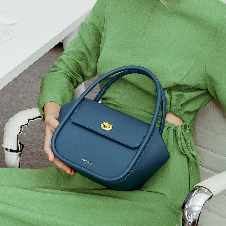 Person holding a blue handbag with a gold clasp, wearing a green outfit.