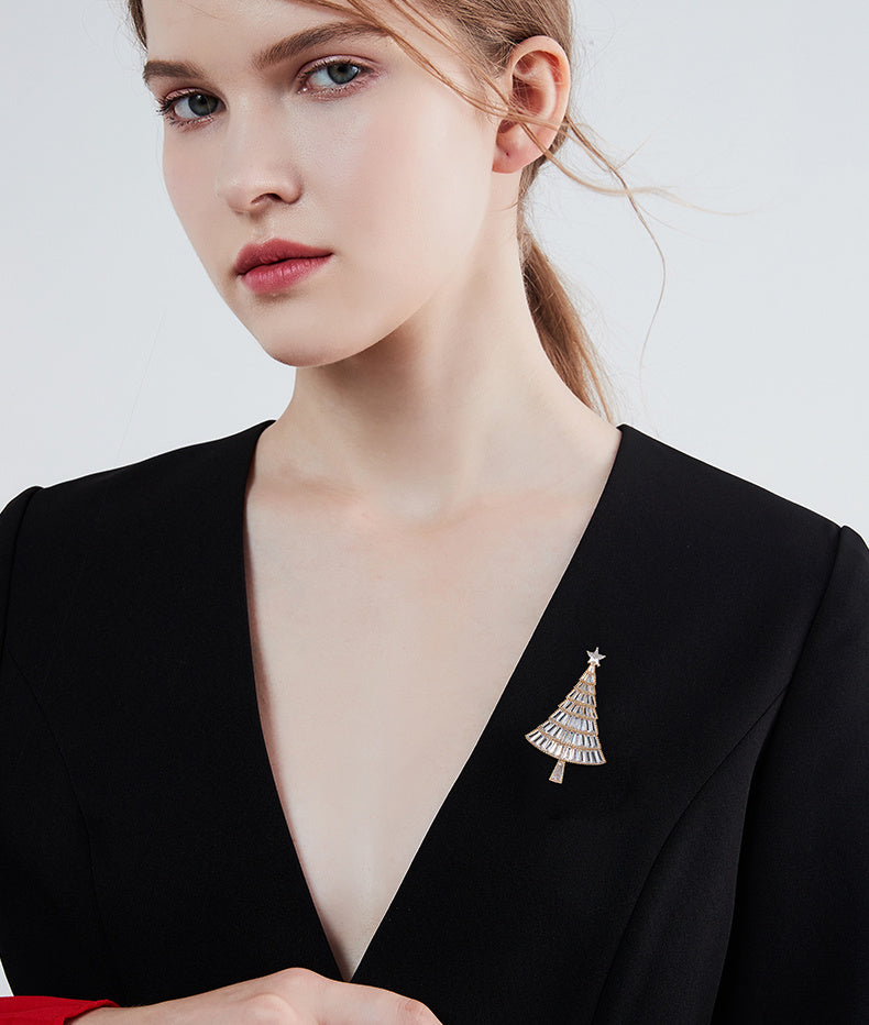 Woman wearing a black blazer with a silver tree-shaped brooch on a white background