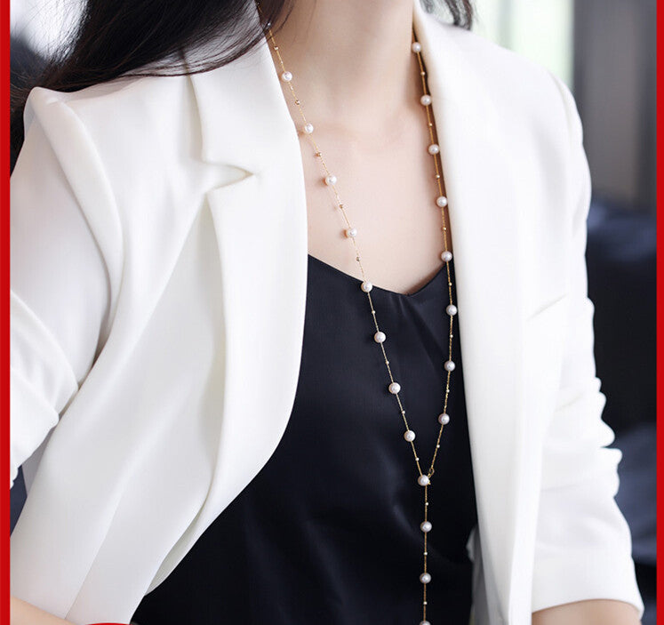Person wearing a long pearl necklace with a white blazer and black top.