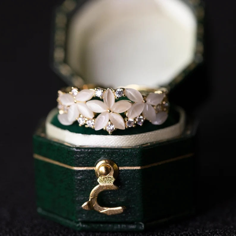 Floral ring with gold accents on a green jewelry box with a gold crescent moon charm.