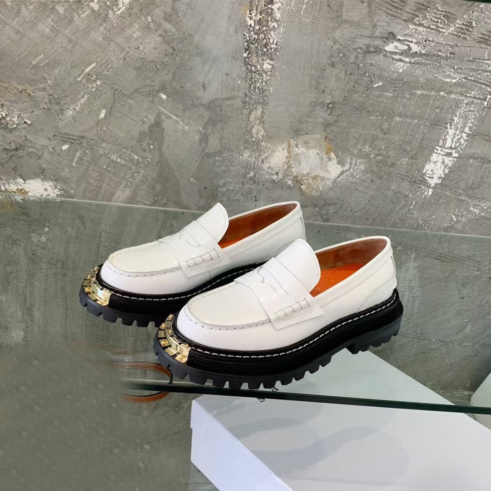 White loafers with black soles on a glass surface against a textured gray background