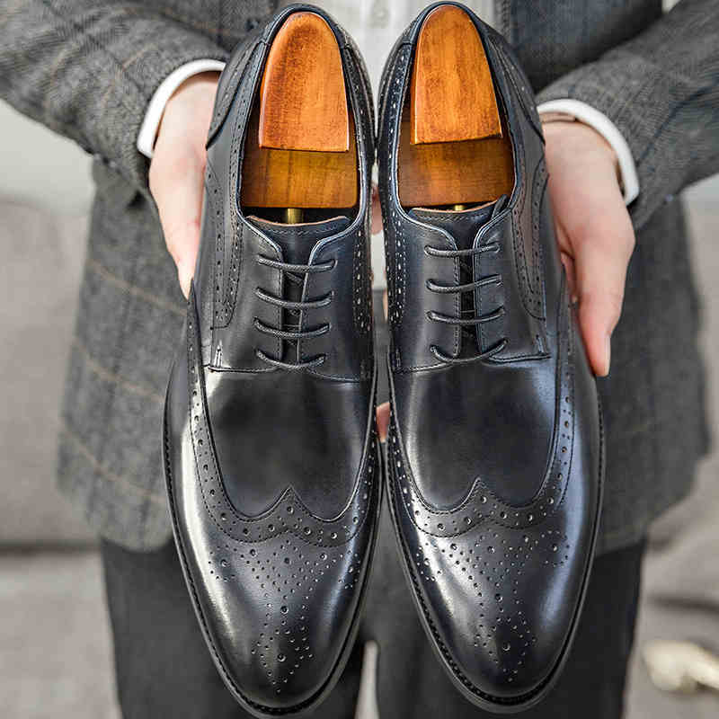 Black leather dress shoes with wooden soles held by a person wearing a gray suit.