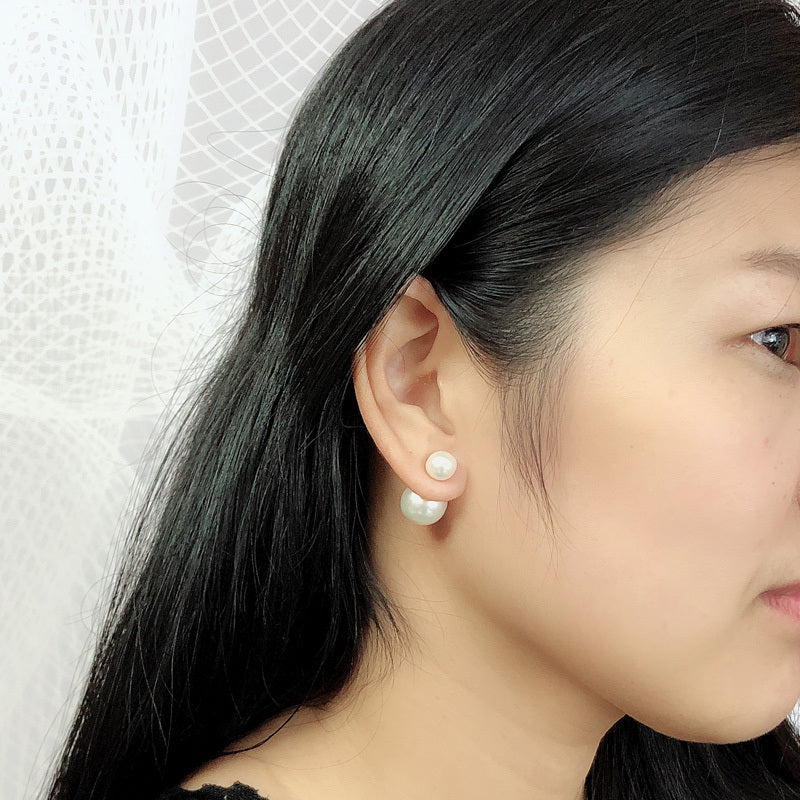 Close-up of a person wearing pearl earrings with a neutral background