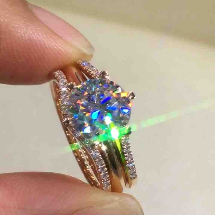 Rose gold ring with a large diamond held between fingers against a neutral background