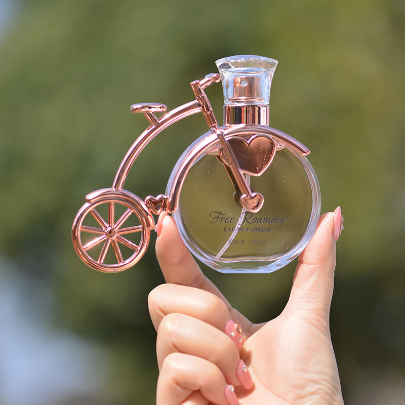Perfume bottle shaped like a bicycle held by a hand with a blurred green background