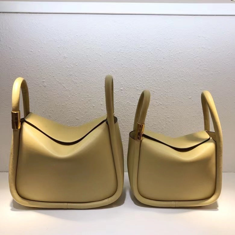 Two beige handbags with gold handles on a white background
