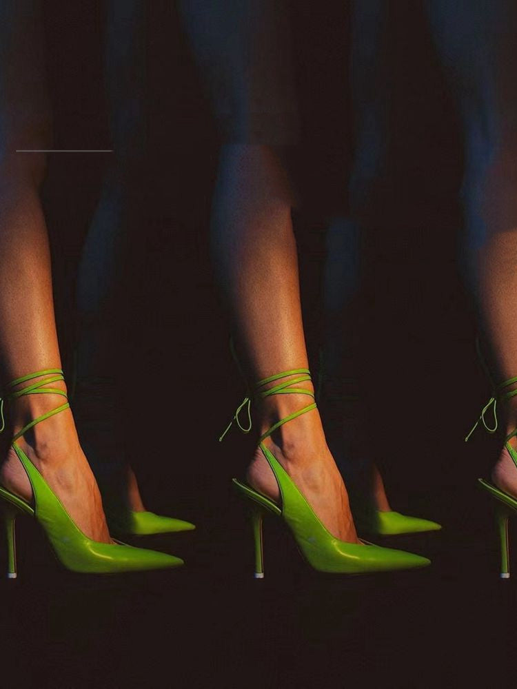 Green high-heeled shoes worn by a person on a dark background