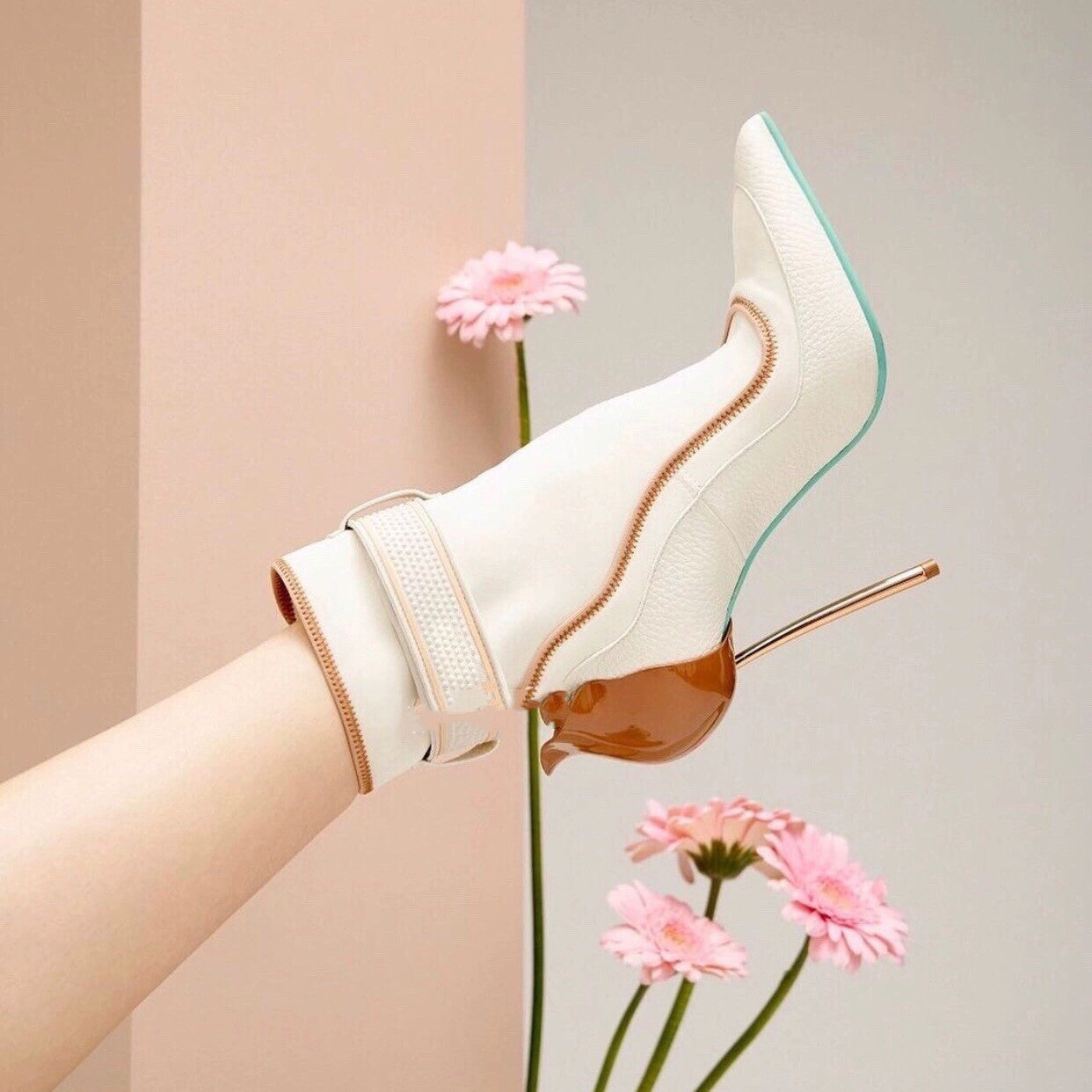 White high-heeled shoe with a pink flower on a neutral background
