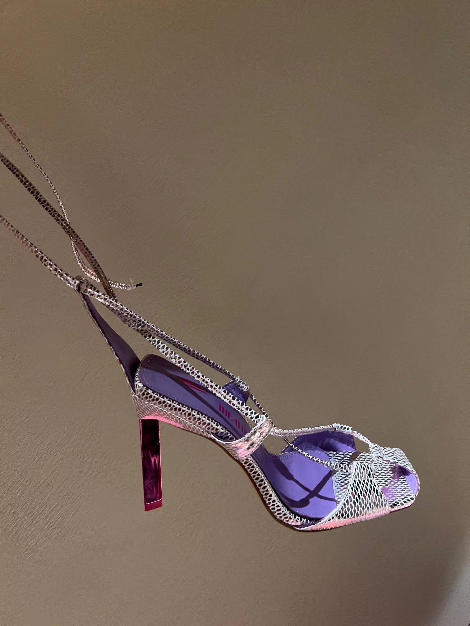 Purple high-heeled shoe with chain detail on a beige background