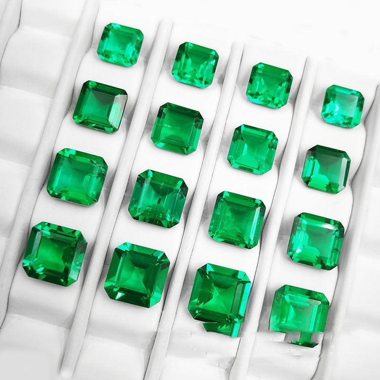 Multiple square-cut emeralds arranged in a grid on a textured white surface.