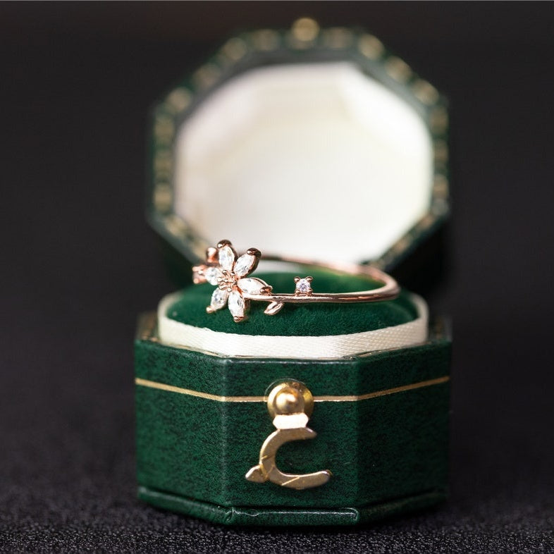 Gold ring with floral design in a green jewelry box on a dark background