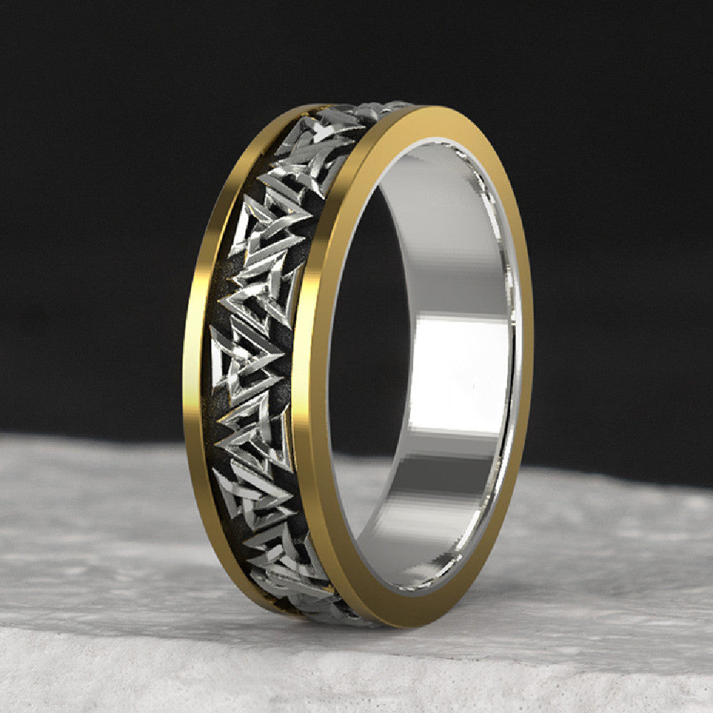 Gold and silver ring with intricate design on a dark background
