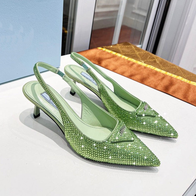 Green studded high-heeled shoes on a white surface with a mirror and orange cushion in the background.