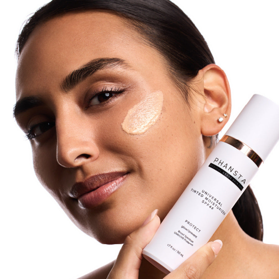 Woman applying PHANSTA skincare product to her face with a white background
