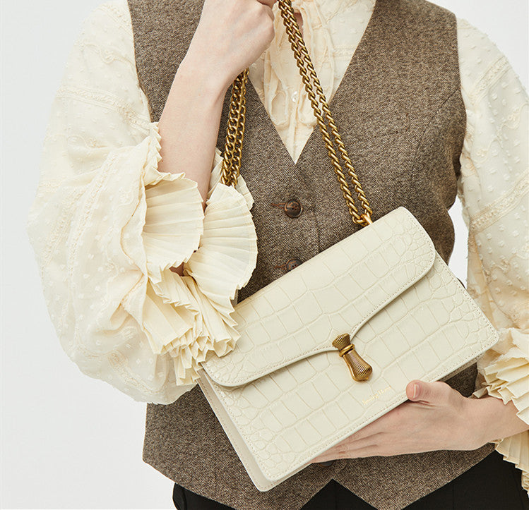 Person holding a cream-colored handbag with a gold chain strap against a neutral background