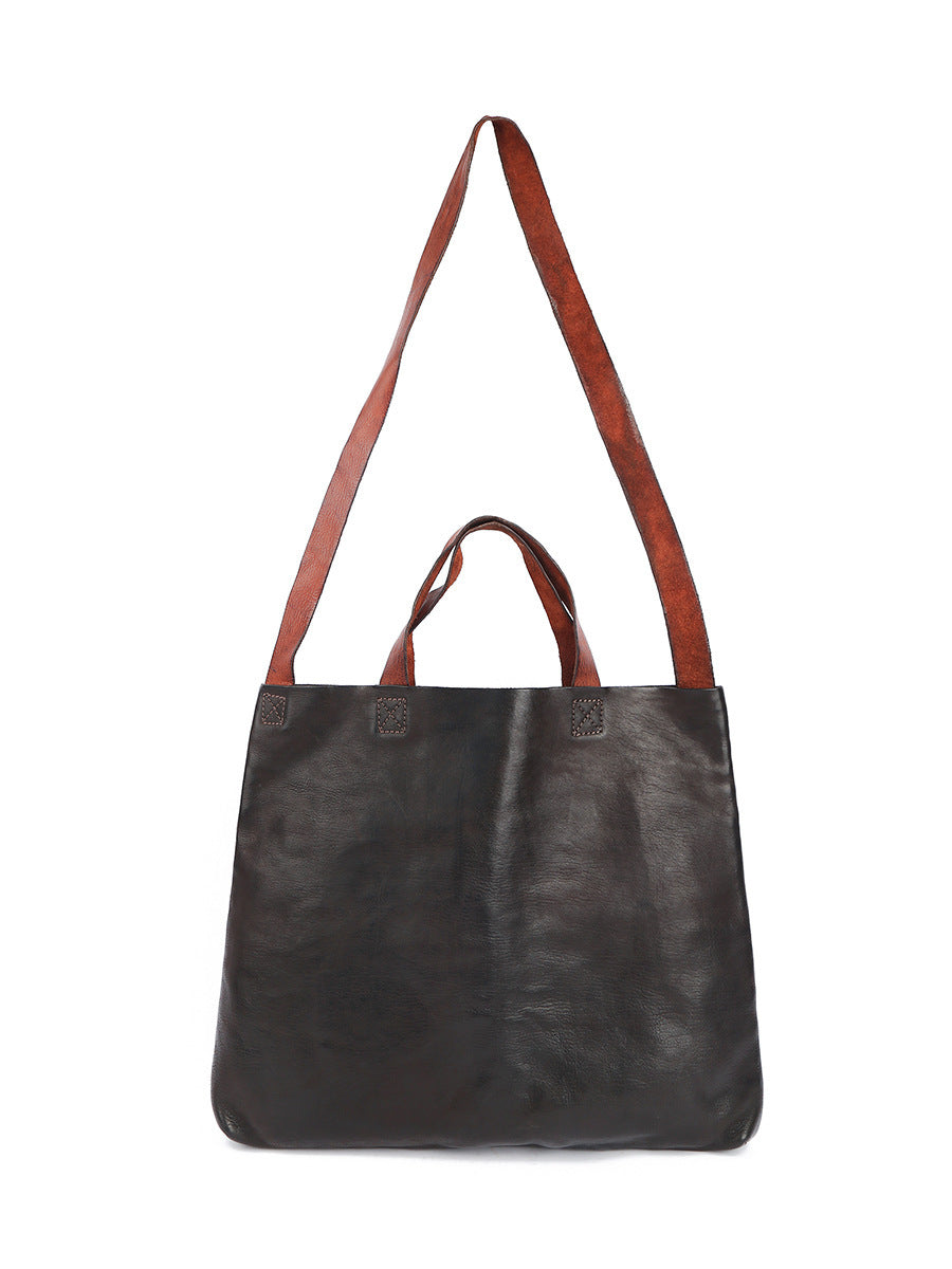 Black leather tote bag with brown straps on a white background