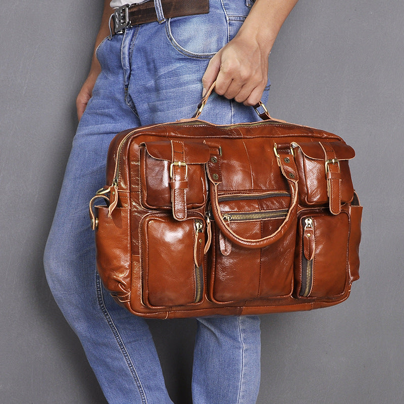 Brown leather bag held by a person wearing blue jeans against a gray background