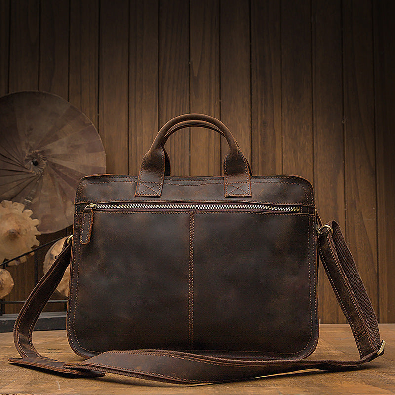 Brown leather briefcase with shoulder strap on a wooden surface with a wooden panel background