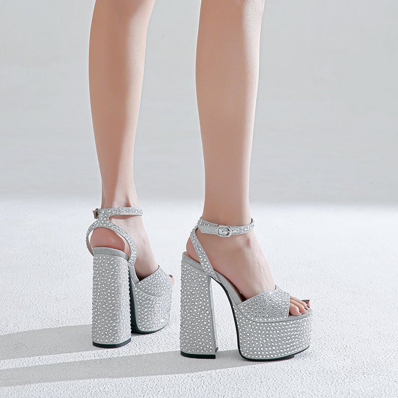 Silver high-heeled platform shoes with rhinestone details on a white background