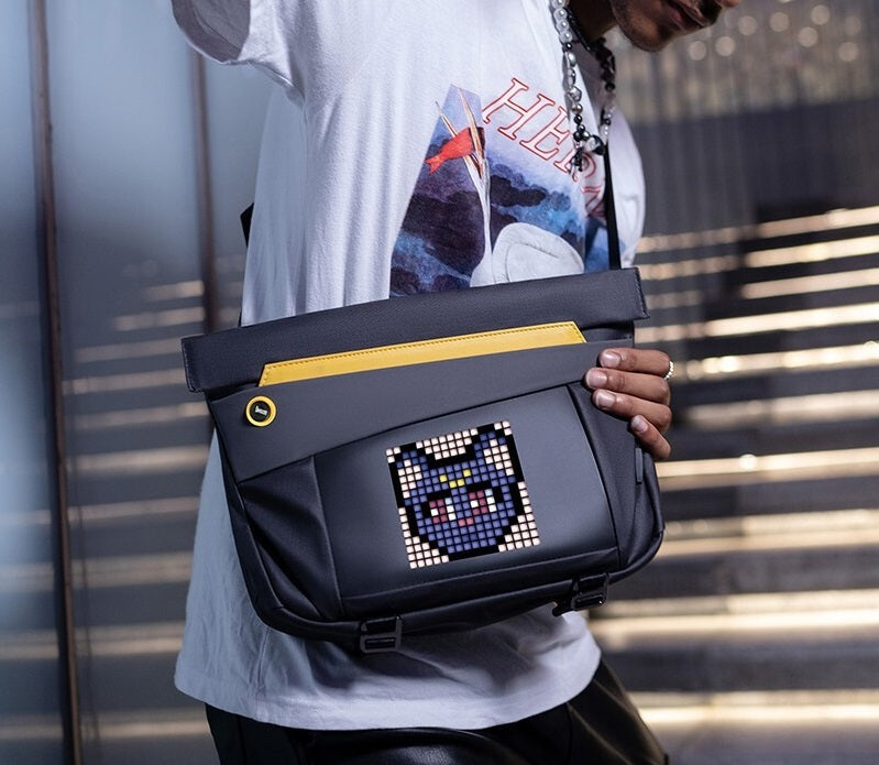 Person holding a black and yellow bag with a pixelated design, wearing a white t-shirt with a graphic print.