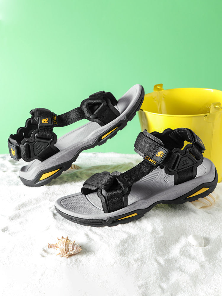 Black and gray sandals with yellow accents on a sandy surface with a green background