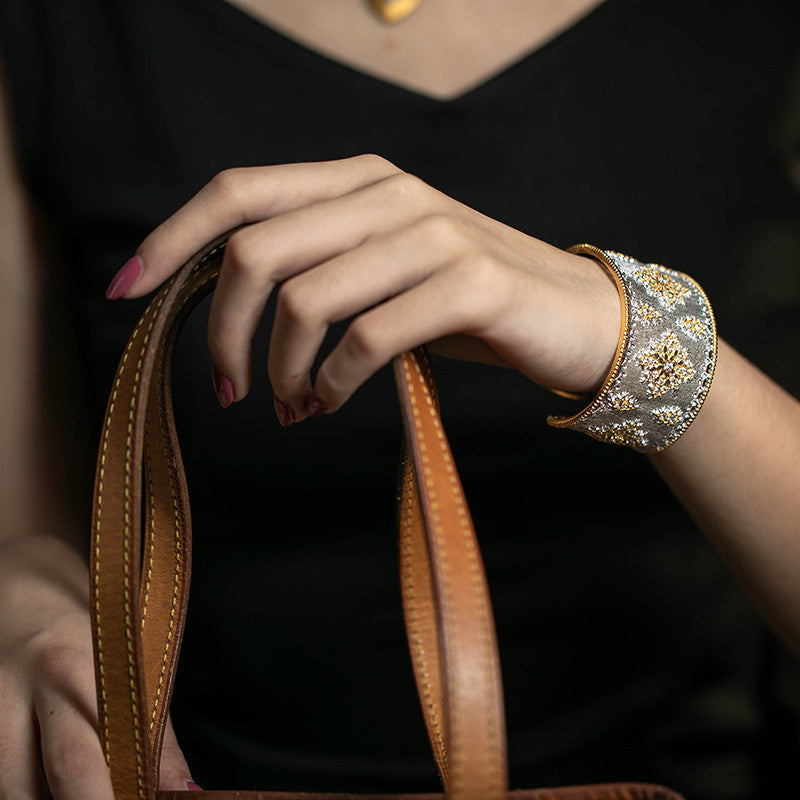 Hand holding a brown leather bag with a decorative cuff on a dark background