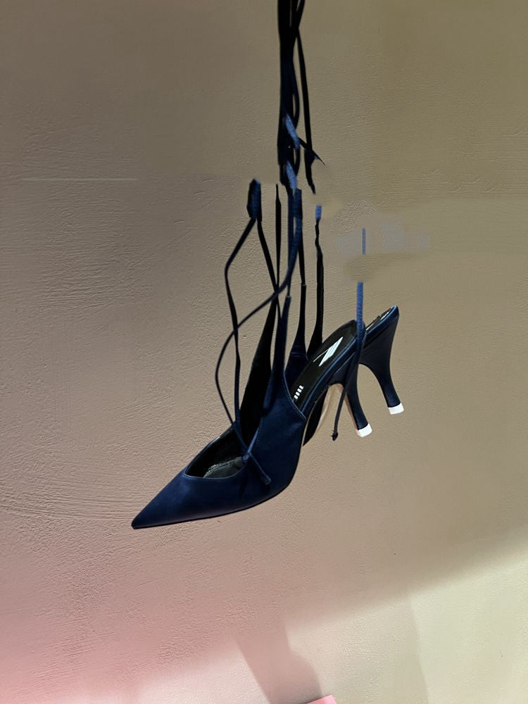Pair of blue high-heeled shoes with thin straps hanging against a beige wall.