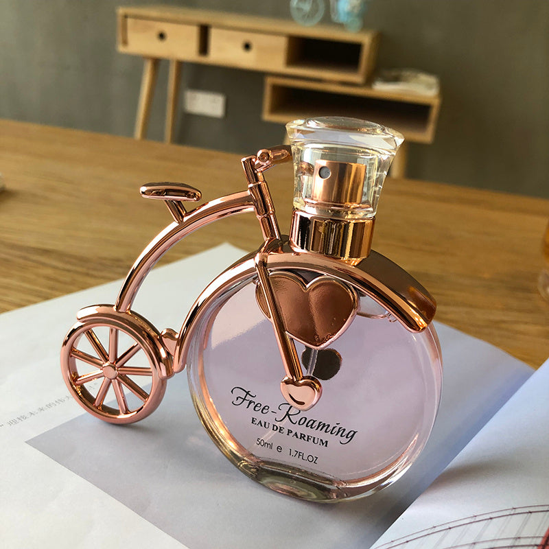 Perfume bottle shaped like a bicycle with rose gold accents on a table.