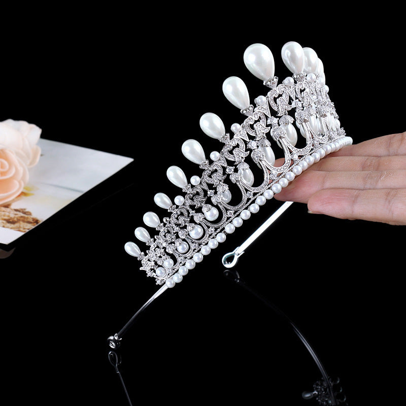 Silver tiara with pearls held by a hand on a black background