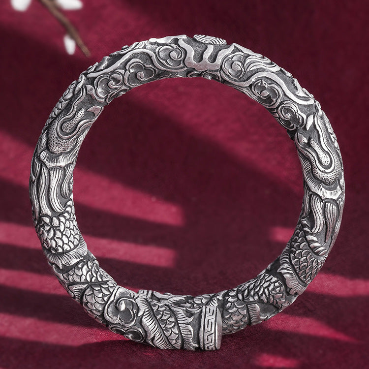 Silver bracelet with intricate designs on a red fabric background