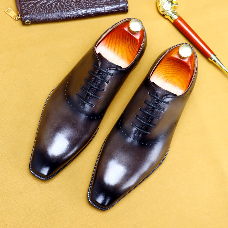 Pair of black dress shoes with orange soles on a yellow background