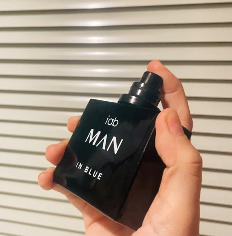Hand holding a black perfume bottle labeled 'iab MAN IN BLUE' against a neutral background