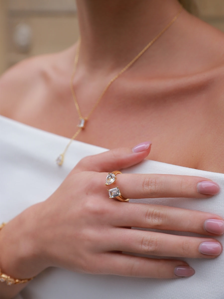 Close-up of a person wearing gold jewelry with pink nail polish on a neutral background