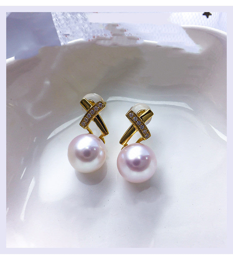 Pearl earrings with gold cross designs on a white dish