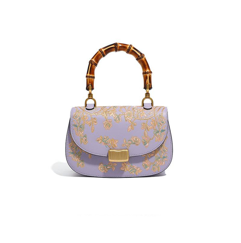 Lavender handbag with gold floral embroidery and bamboo handle on a white background