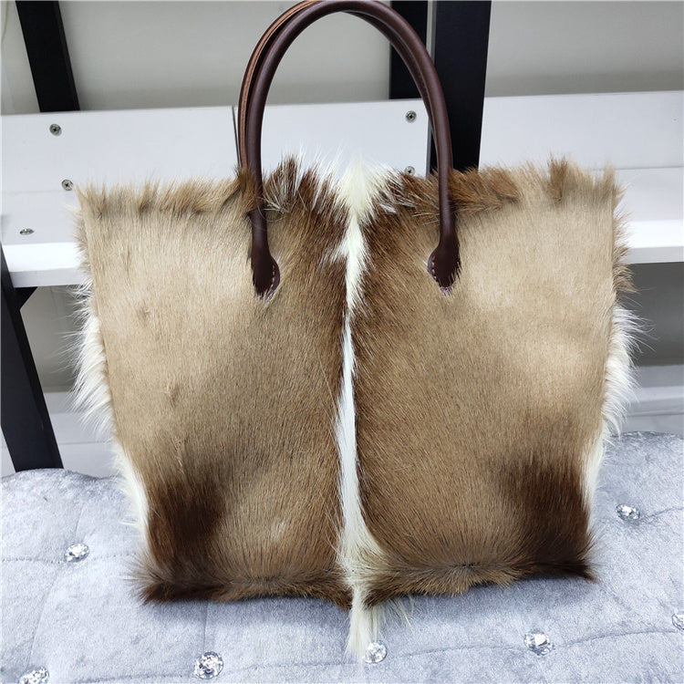 Brown and beige fur tote bag with leather handle on a textured surface