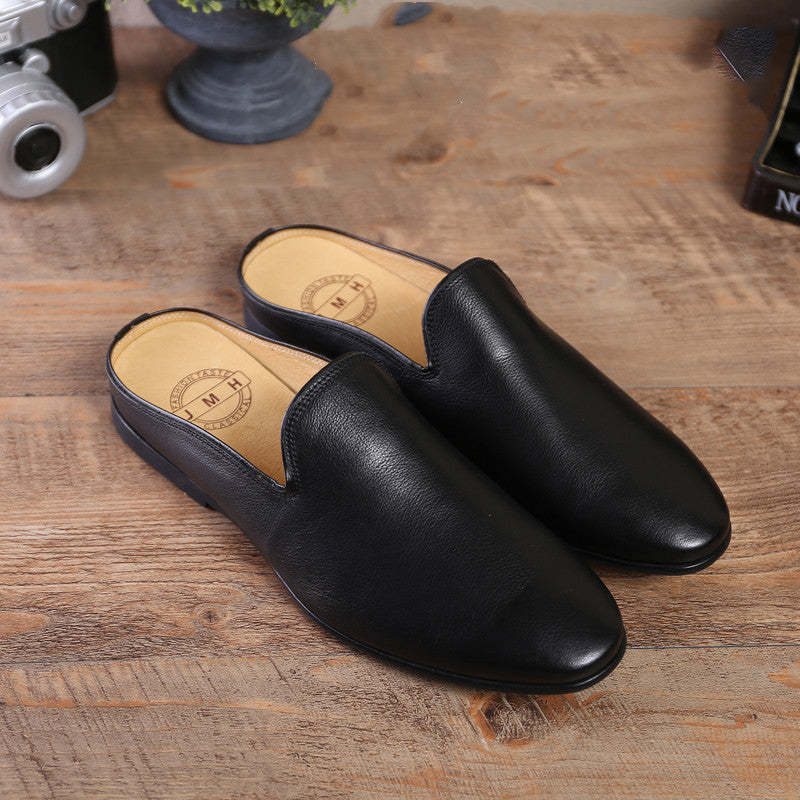 Pair of black leather slippers on a wooden surface with a camera and plant in the background.