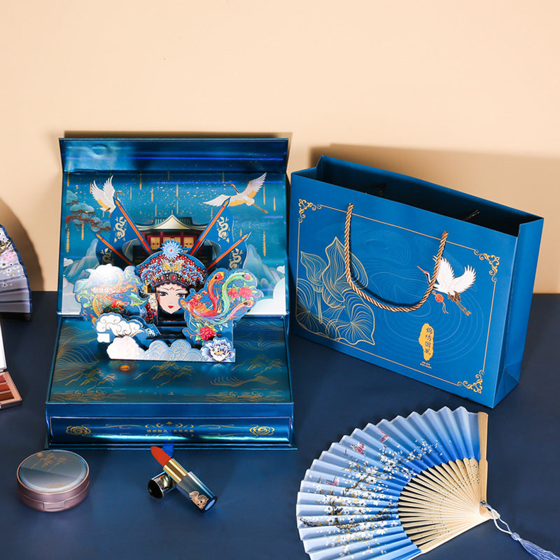 Blue decorative box with artistic design, fan, and lipstick on a dark surface