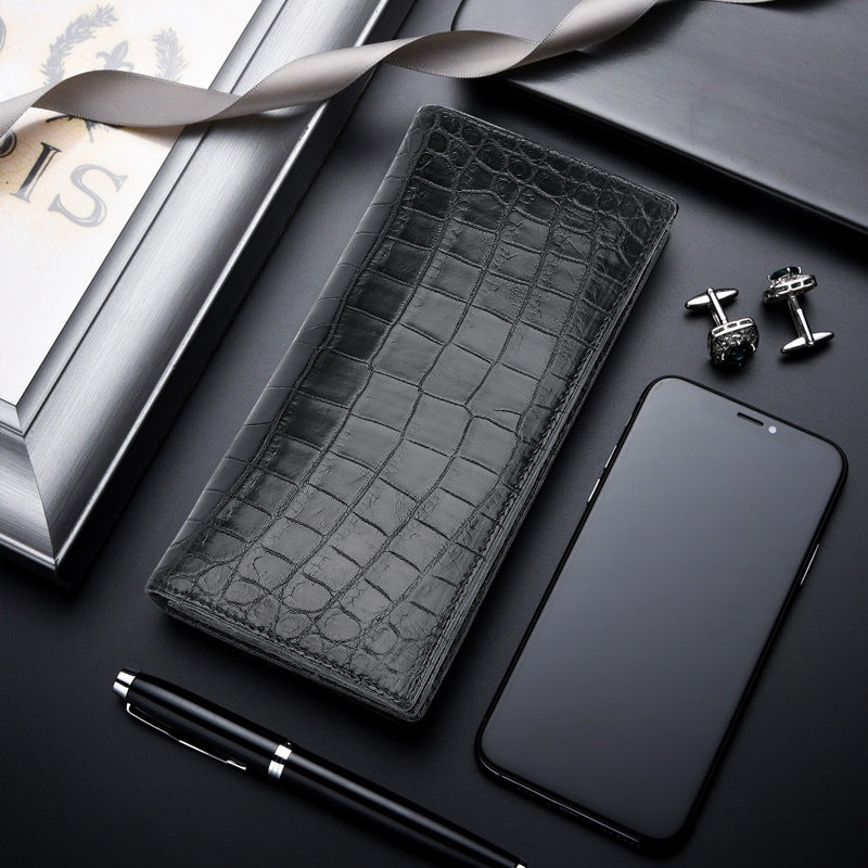 Black crocodile-patterned wallet, phone, pen, and cufflinks on a dark surface with a magazine.