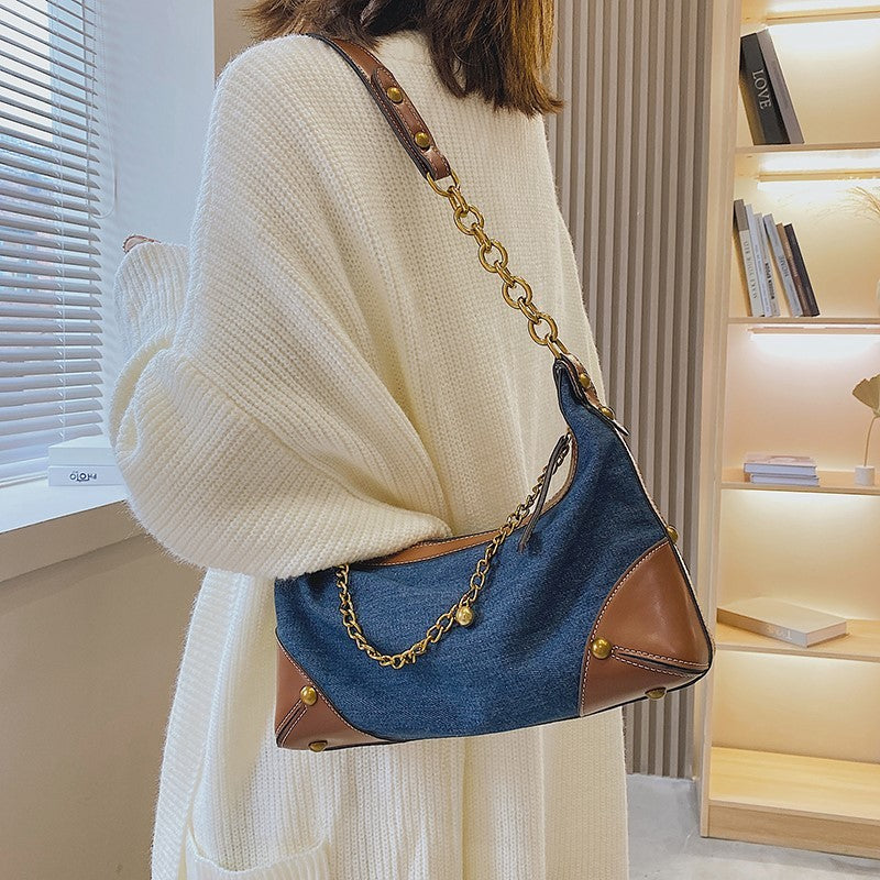 Person wearing a white sweater holding a blue handbag with gold chain strap in a room.