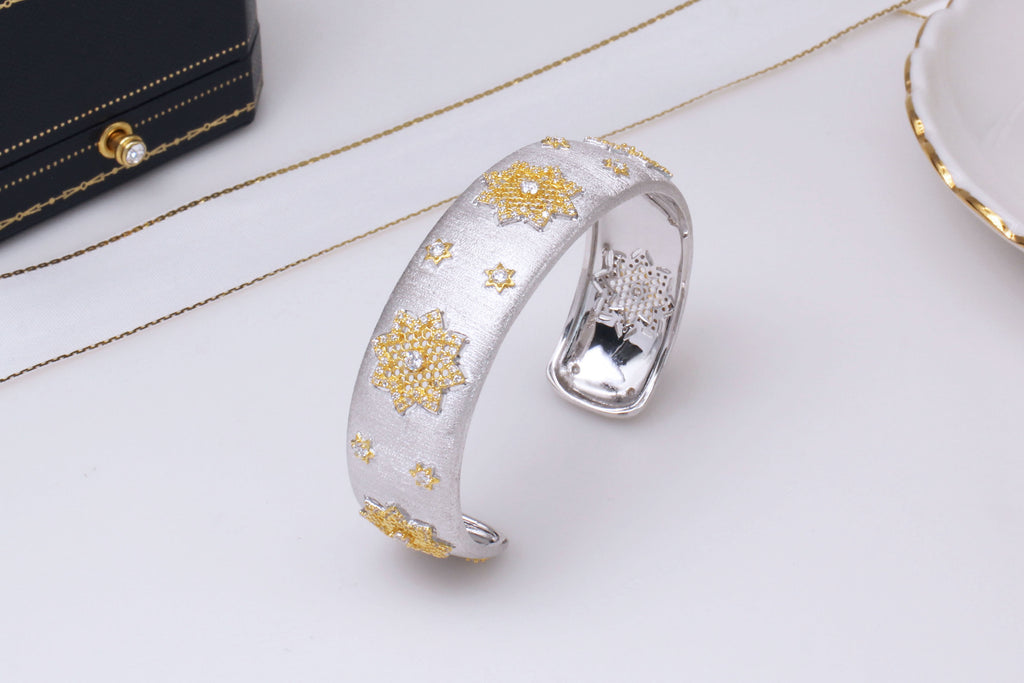 Silver bracelet with gold floral designs on a white surface