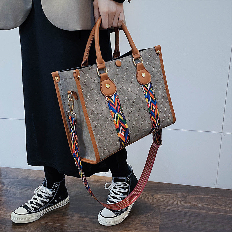 Person holding a gray handbag with a colorful strap, wearing black sneakers.