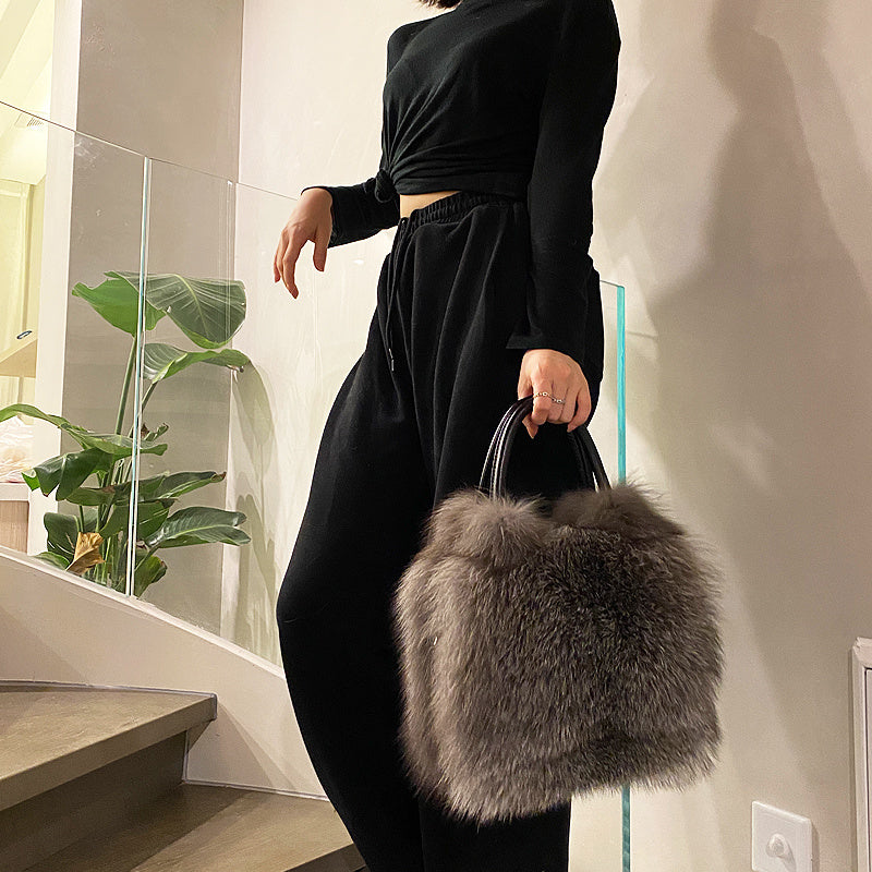 Person holding a fluffy gray handbag indoors