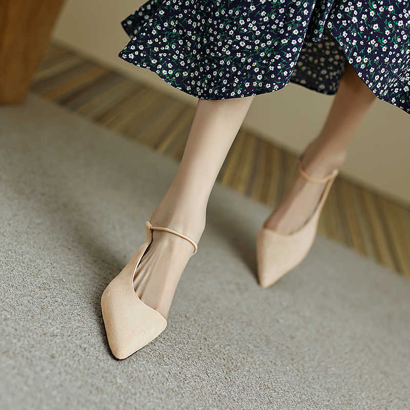 Beige pointed-toe shoes worn with a floral dress on a neutral background